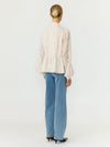 A woman viewed from the back wearing a cream-colored textured lace blouse with balloon sleeves and light blue wide-leg jeans, set against a plain white studio background.