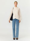 A model stands against a plain light gray studio background wearing a cream lace long-sleeve blouse, light blue straight-leg jeans, black pointed shoes, and carrying a black shoulder bag.