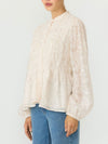 A woman wearing a cream-colored, long-sleeved lace blouse with a gathered smocked bodice and blue jeans, shown from the chin down against a plain light background.