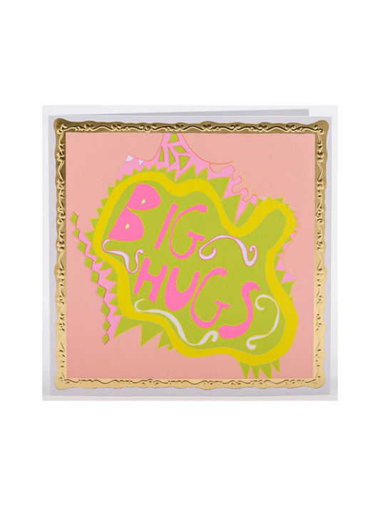 A square greeting card featuring a pink background with a decorative gold border and a central green and pink abstract shape that reads 'BIG HUGS'.
