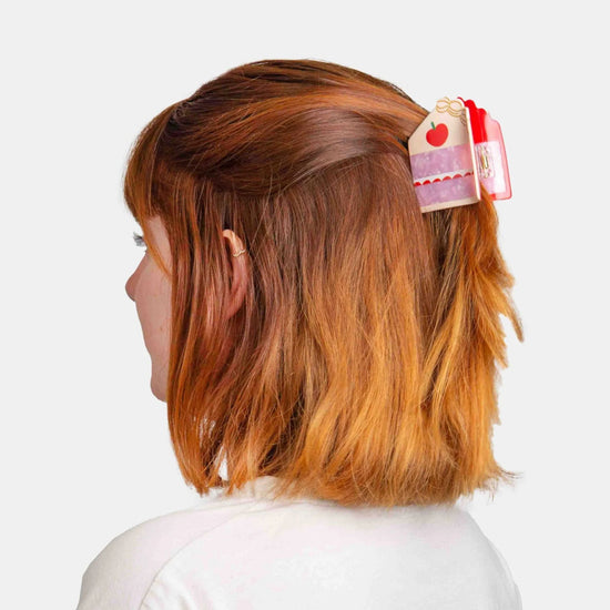 Person with red hair wearing a decorative cake shaped  hair clip on a white background