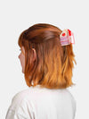 Person with red hair wearing a decorative cake shaped  hair clip on a white background