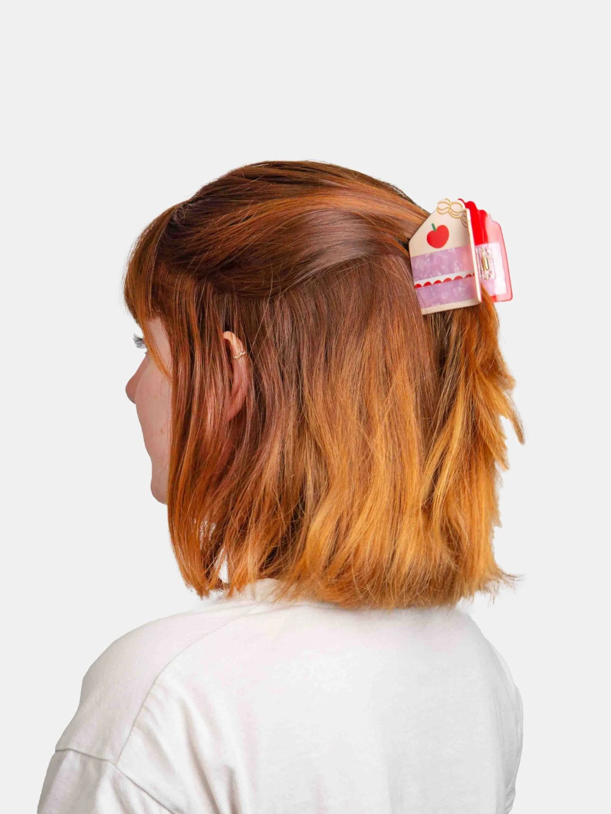 Person with red hair wearing a decorative cake shaped  hair clip on a white background