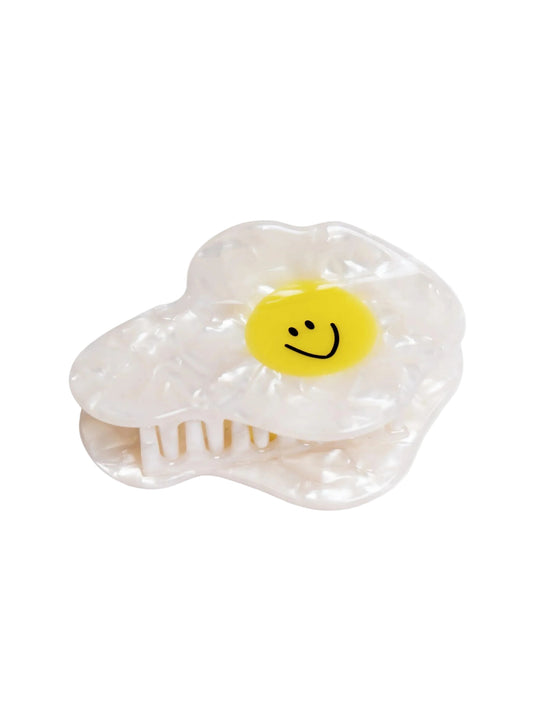 Clear plastic hair clip shaped like a fried egg with a smiley face on a white background