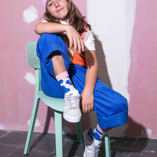 Child sitting on a green chair against a pink wall wearing blue cow print socks