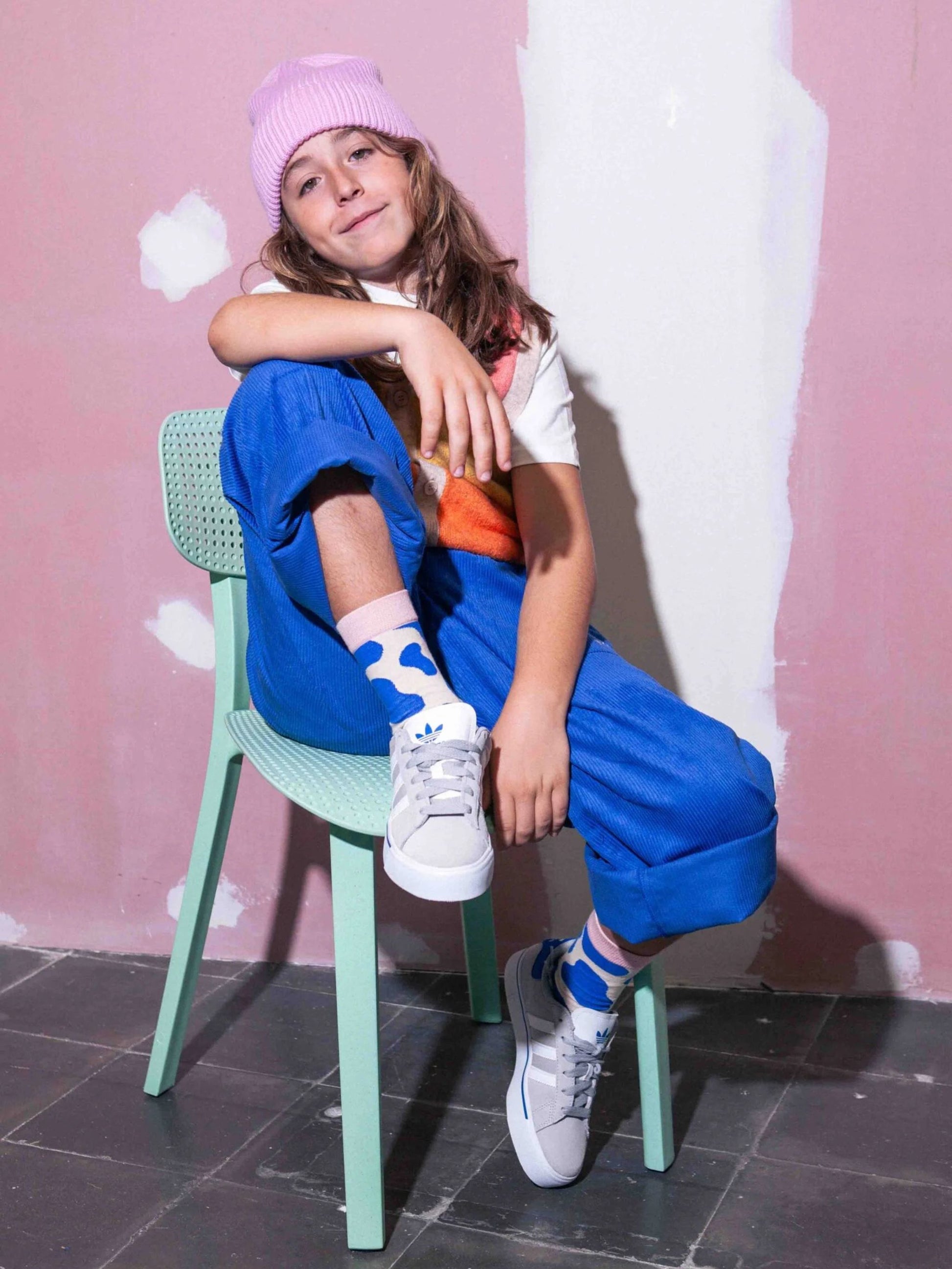 Child sitting on a green chair against a pink wall wearing blue cow print socks