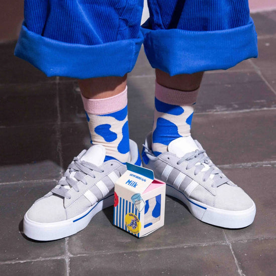 child wearing blue and white cow patterned socks with gray sneakers on a tiled floor.