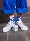 child wearing blue and white cow patterned socks with gray sneakers on a tiled floor.