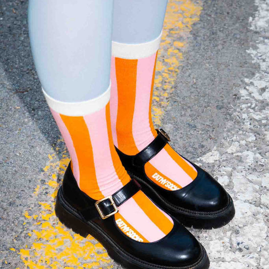 Black shoes with orange and pink striped socks on a road surface