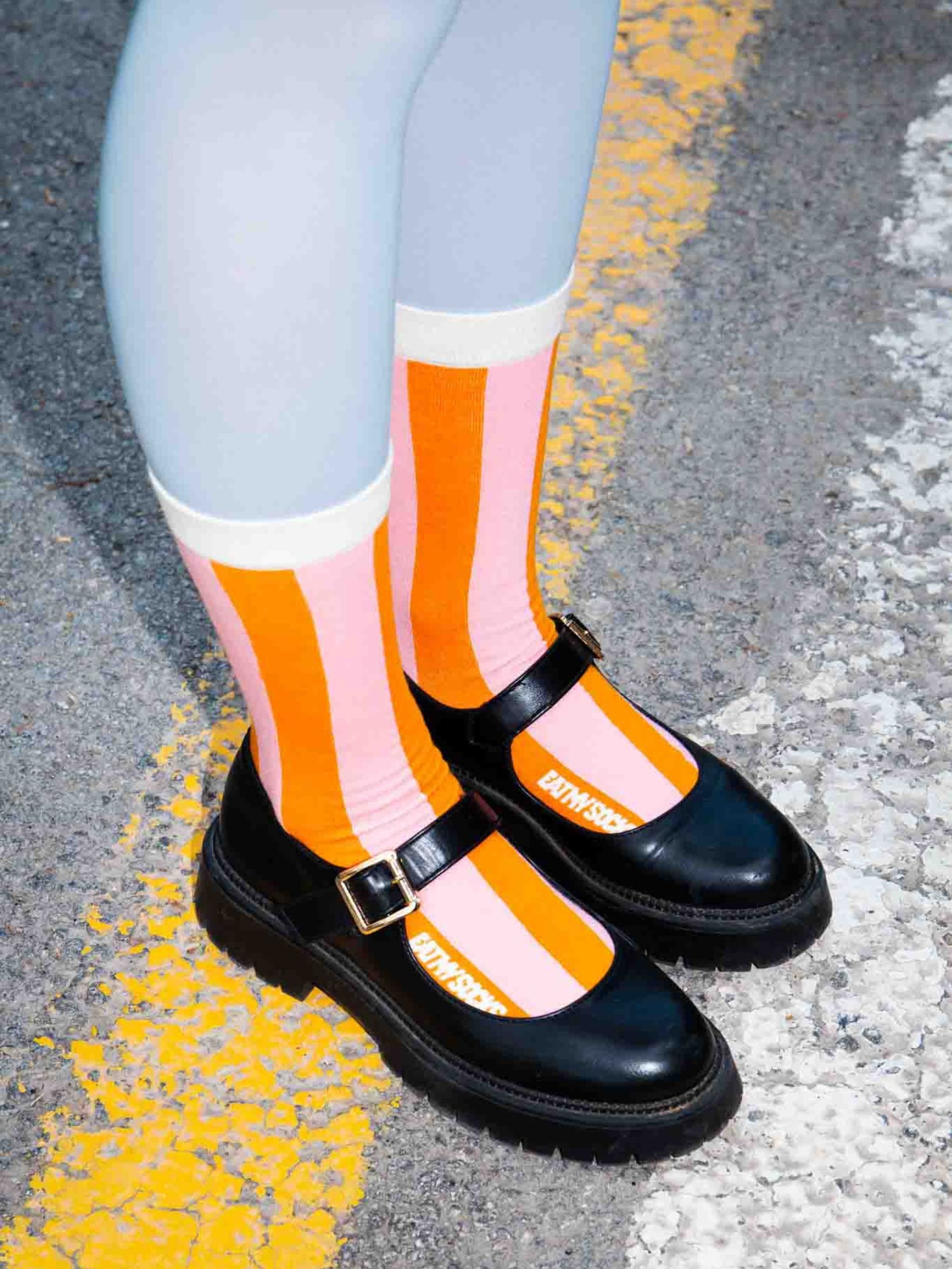 Black shoes with orange and pink striped socks on a road surface