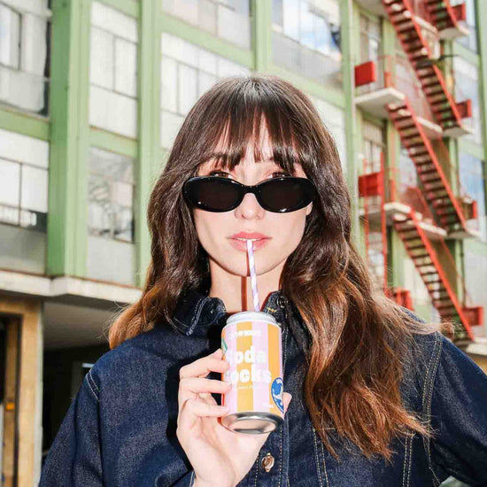 Woman pretending to drink from a soda can with a straw in an urban setting