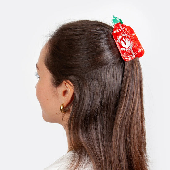 Person with a red and green hot sauce shaped hair clip in their hair on a white background