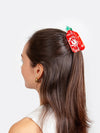 Person with a red and green hot sauce shaped hair clip in their hair on a white background