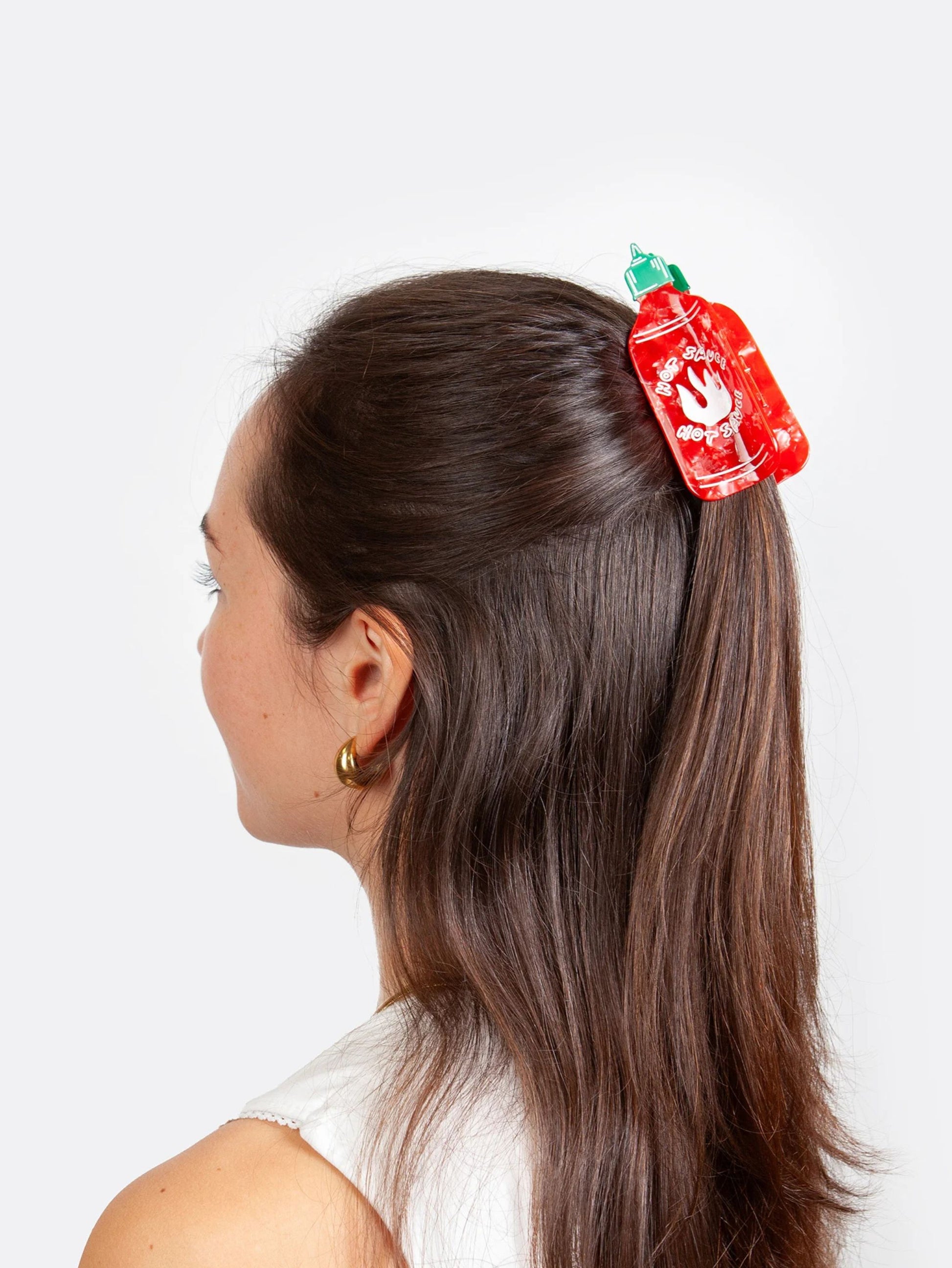 Person with a red and green hot sauce shaped hair clip in their hair on a white background