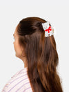 Person with long brown hair wearing a white cat shaped hair clip with a red bow on a light gray background