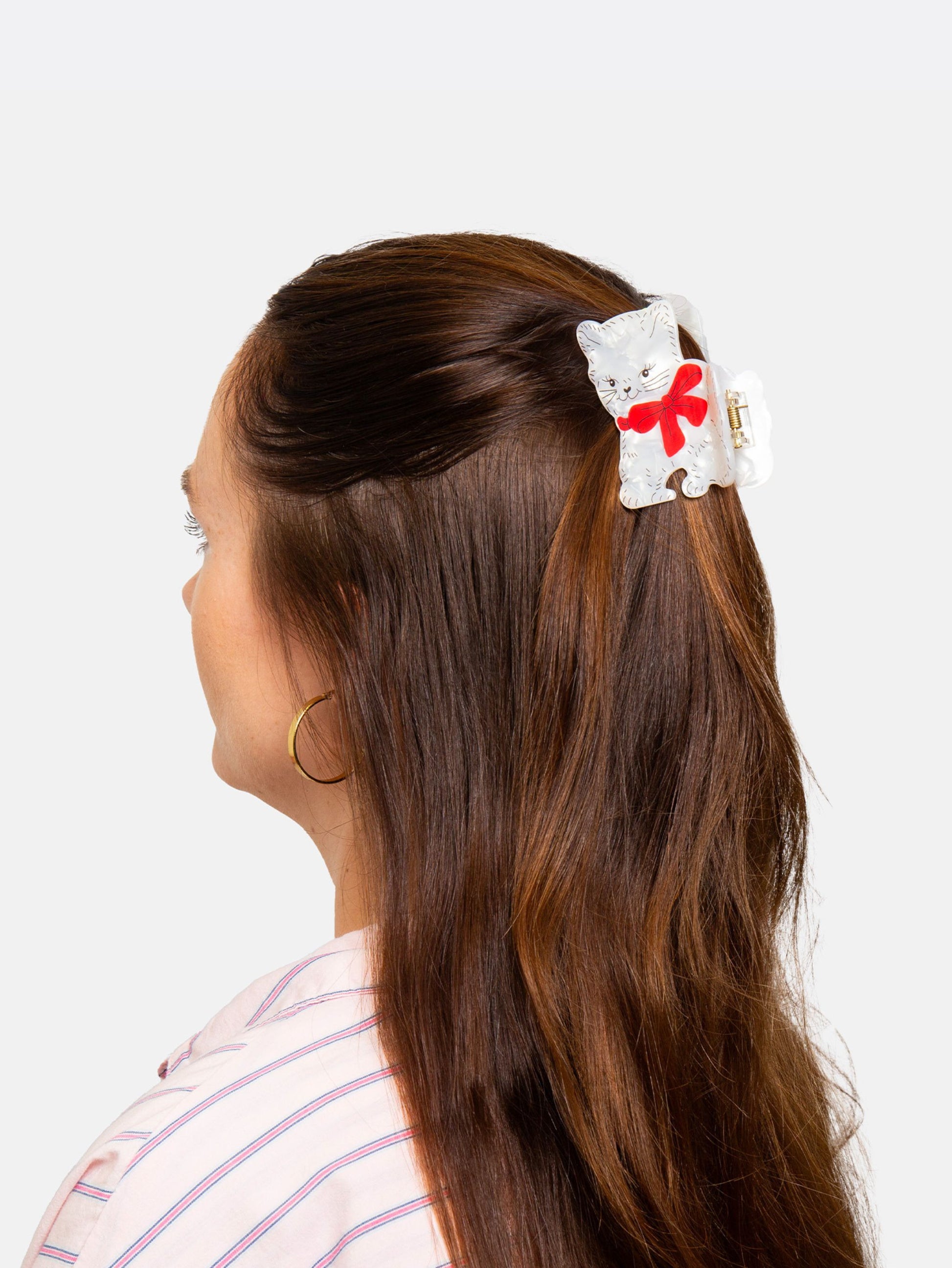 Person with long brown hair wearing a white cat shaped hair clip with a red bow on a light gray background