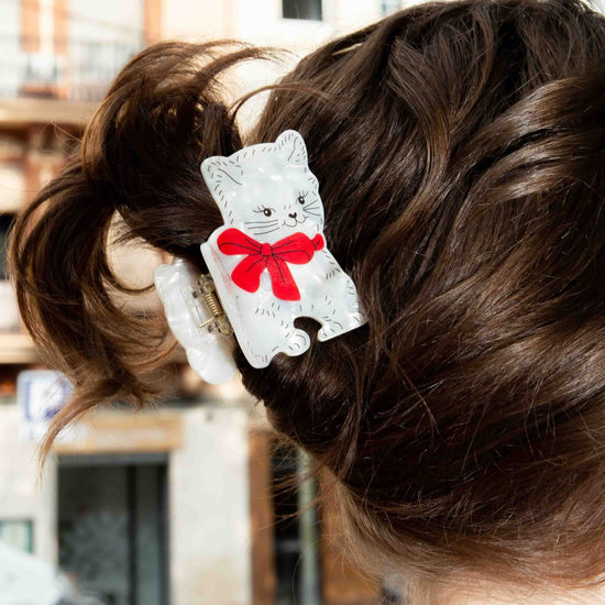 Hair clip with a cat design and red bow in a person's hair, blurred city street background