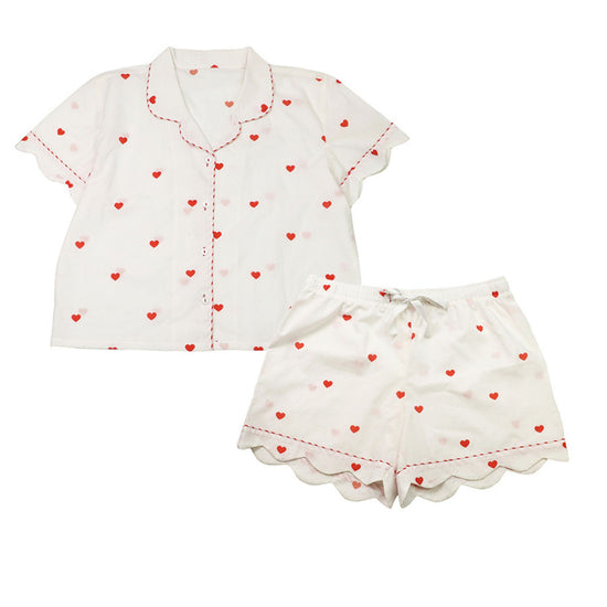 A two-piece women's pyjama set featuring a short-sleeve button-up top and matching shorts in white, both decorated with a small red heart pattern and scalloped edges.