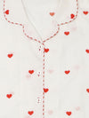 Close-up of a white pyjama top with red heart prints, red-and-white striped piping along the collar and placket, and white buttons.