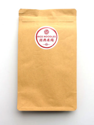 A kraft paper stand-up pouch with a circular red and white label reading 'RICE NOODLES' and Chinese characters, photographed on a plain white background.