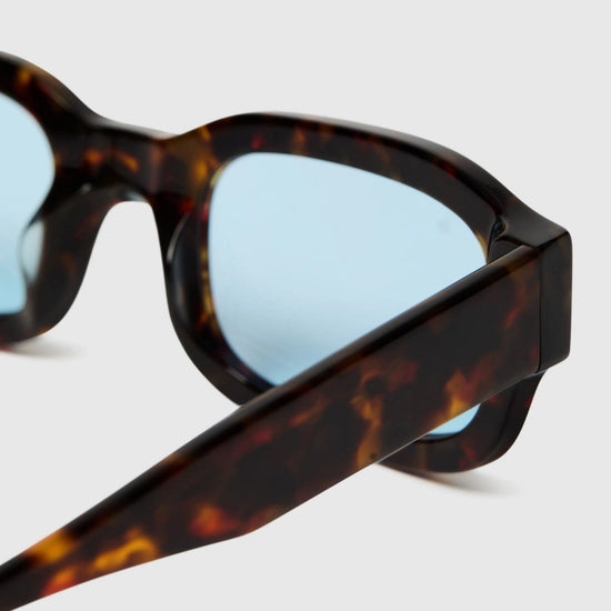Sunglasses with tortoiseshell frame and blue lenses on a white background