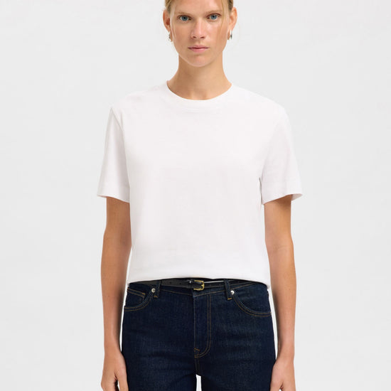 Person wearing a white t-shirt and dark jeans with belt on a plain background