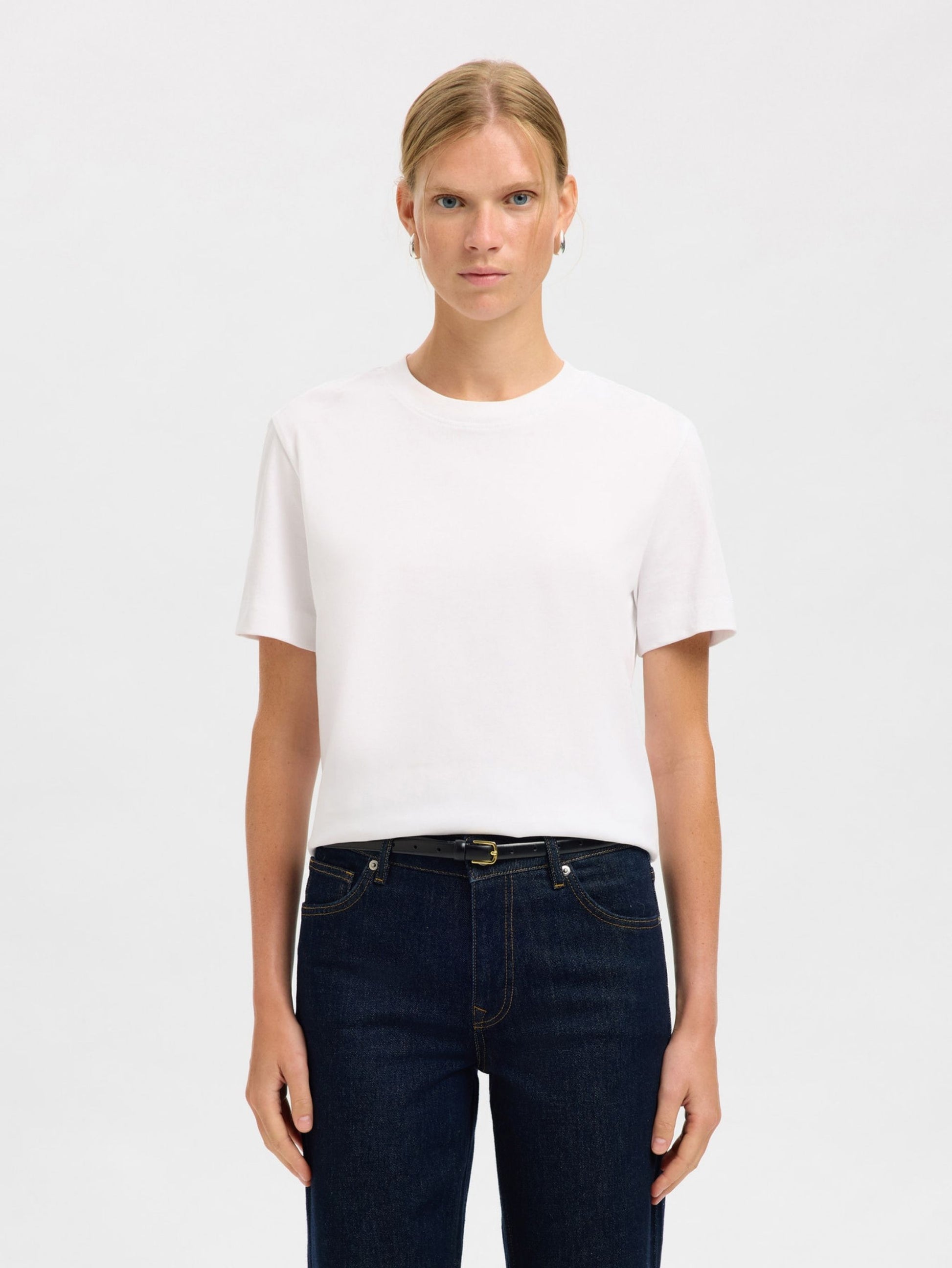 Person wearing a white t-shirt and dark jeans with belt on a plain background