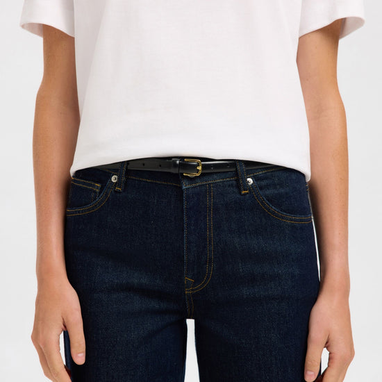 Person wearing dark blue jeans with belt and a white t-shirt on a plain background