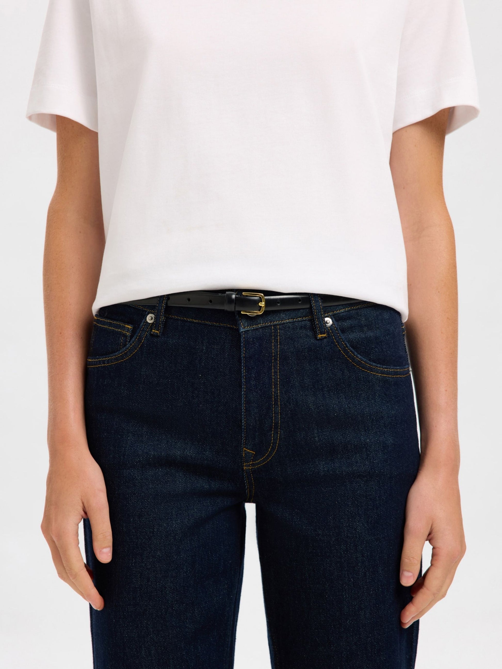 Person wearing dark blue jeans with belt and a white t-shirt on a plain background