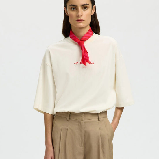 Woman wearing a white blouse with a red scarf and beige pants on a light gray background
