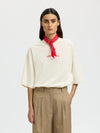 Woman wearing a white blouse with a red scarf and beige pants on a light gray background