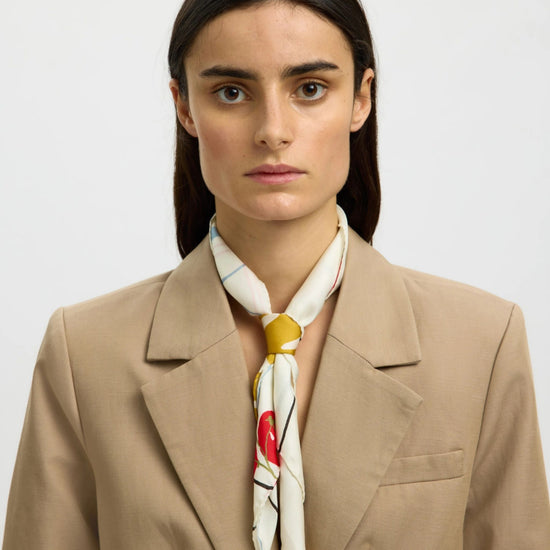 Woman wearing a beige blazer and a colorful scarf against a plain background
