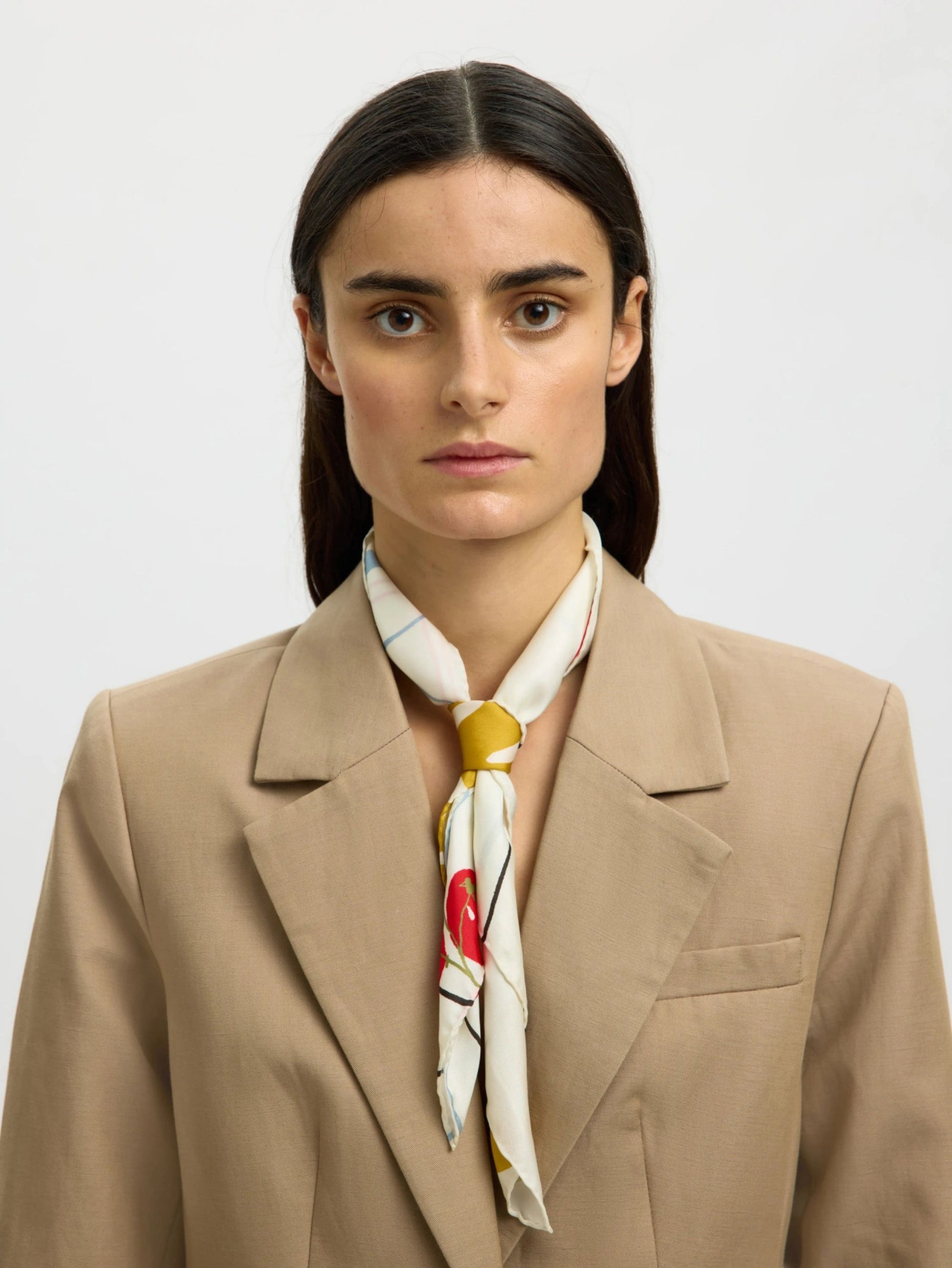 Woman wearing a beige blazer and a colorful scarf against a plain background